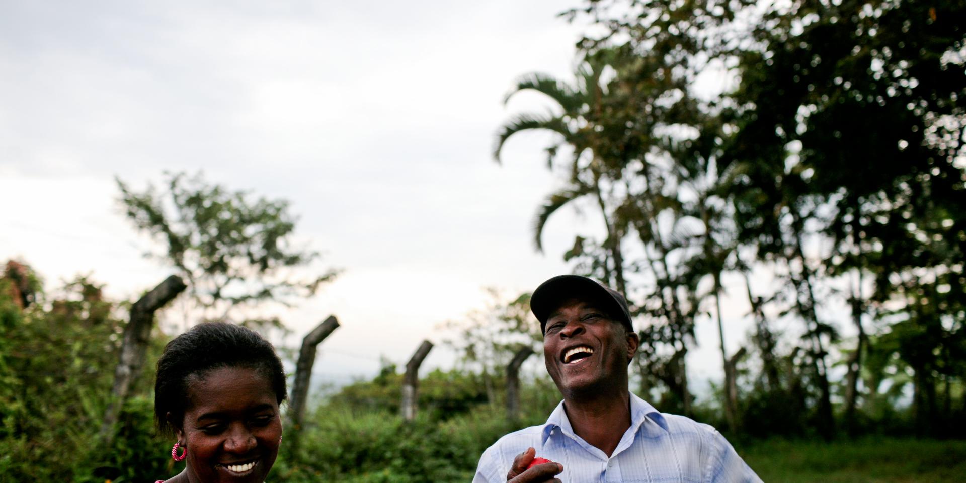 A woman and man laugh together outside next to crops and trees