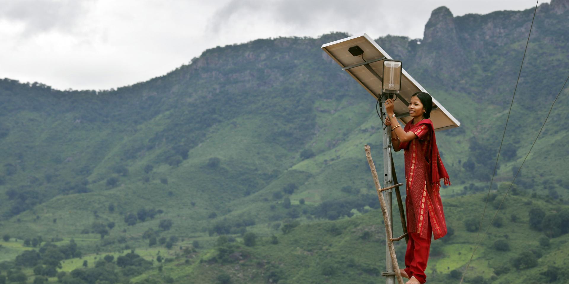 Woman standing on ladder leaning against pole with solar panel
