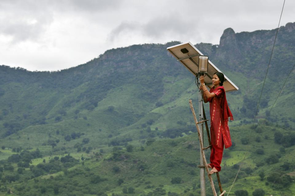 Woman standing on ladder leaning against pole with solar panel