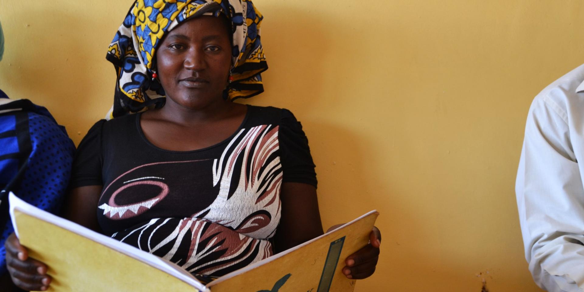 A woman looking at the camera sits in a building reading a book that says 'visitors book'