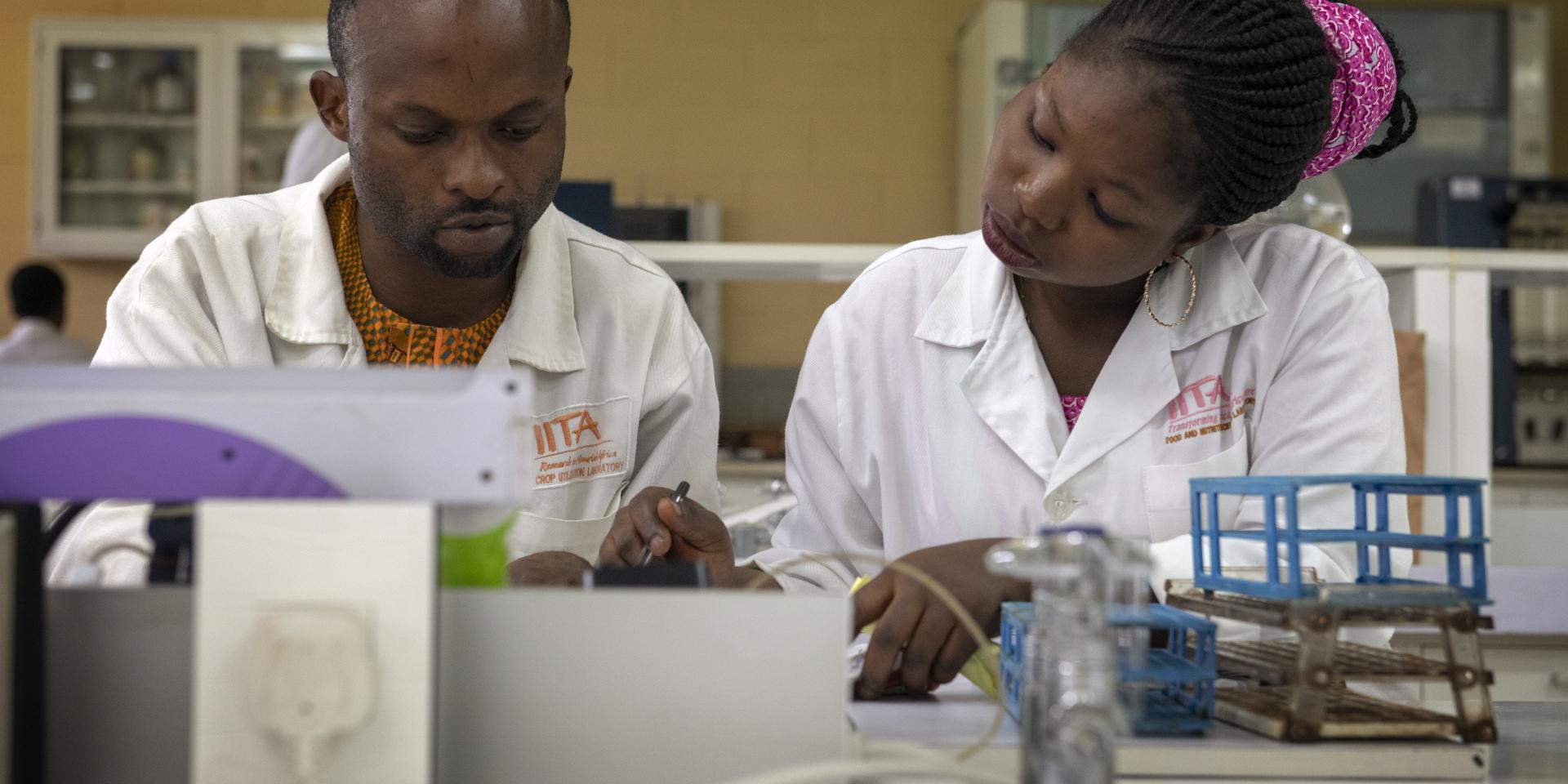 A woman and man sit at a desk in their lab coats, examining a sample