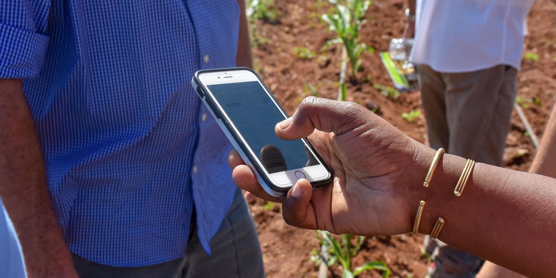 Hand holding cell phone with field in the background