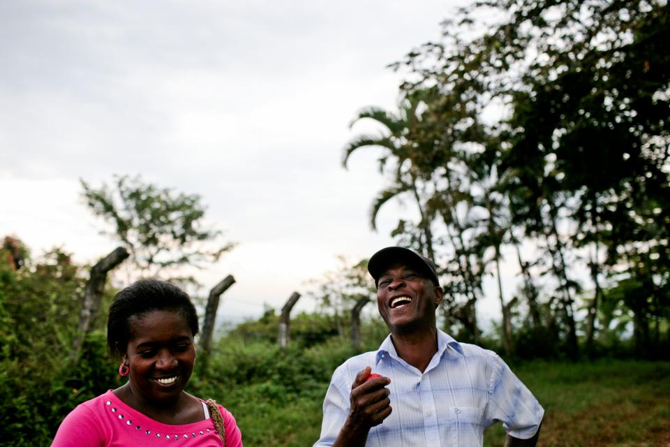 A woman and man laugh together outside next to crops and trees