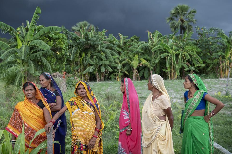 Women farmers walk across a field in front of a blackened rainy sky