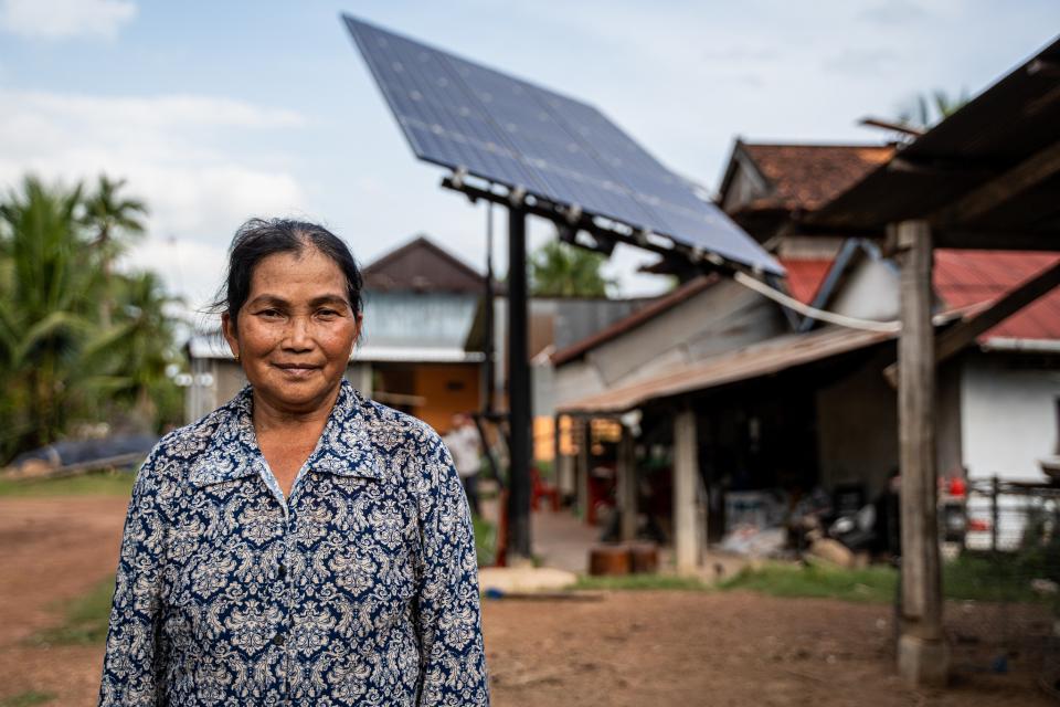 Woman farmer standing infront of a house with solar panels in the backgroung